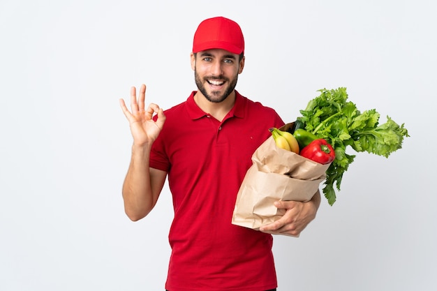 指でokの標識を示す野菜の完全な袋を保持しているひげを持つ男