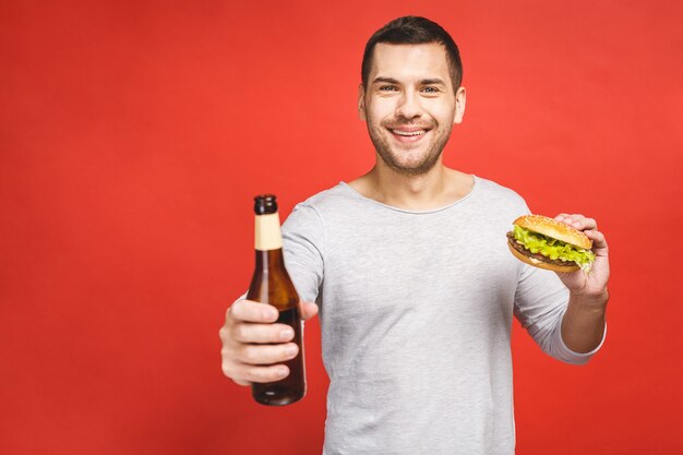 Man with a beard holds a hamburger and a bottle of beer