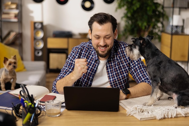 Мужчина с бородой сидит за своим столом со своей собакой и счастлив