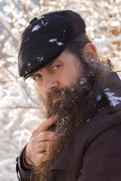 A man with a beard in the snow. Strokes his beard.