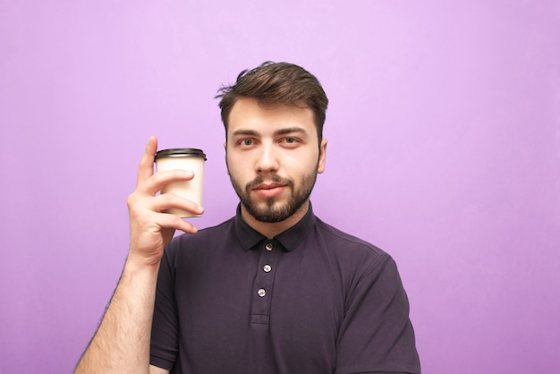 手にコーヒーの紙コップと紫色の背景に立っているひげを持つ男