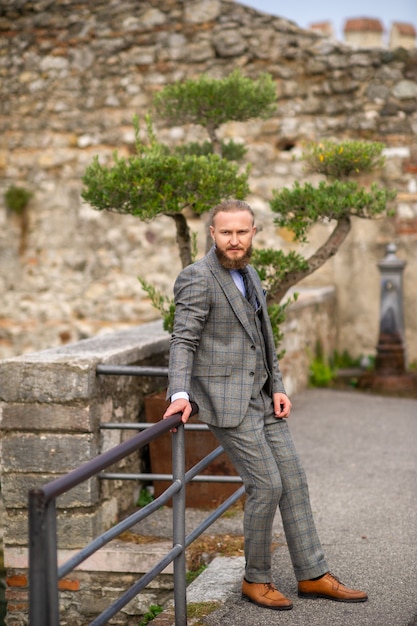 A man with a beard in a strict grey three-piece suit with a tie in the old town of Sirmione.
