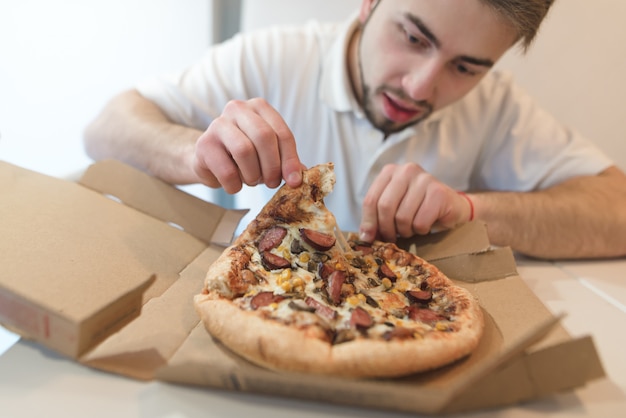 A man with a beard takes a delicious piece of pizza from a cardboard box and looks at her with an appetite.