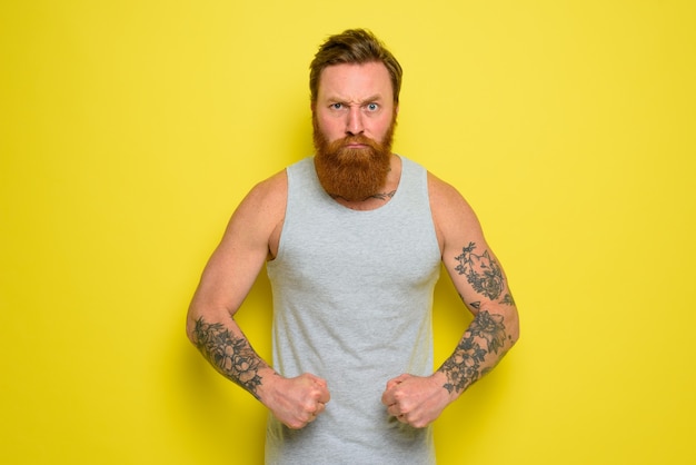 Мужчина с бородой и татуировками с гордостью показывает свои мышцы