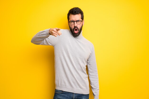 Uomo con barba e collo alto frustrato da una brutta situazione e che punta in avanti