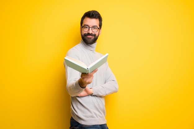 Man with beard and turtleneck holding a book and giving it to someone