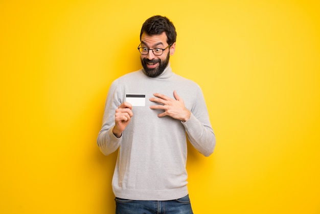 Man with beard and turtleneck holding a credit card and surprised