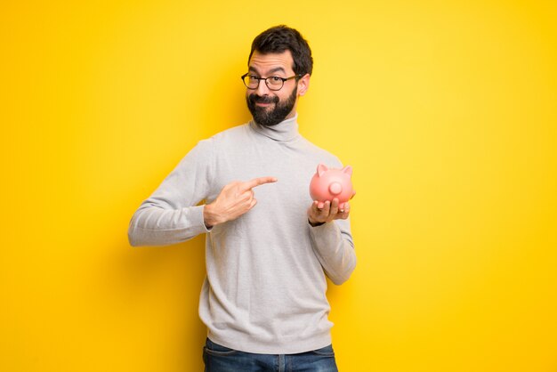 Man with beard and turtleneck holding a piggybank