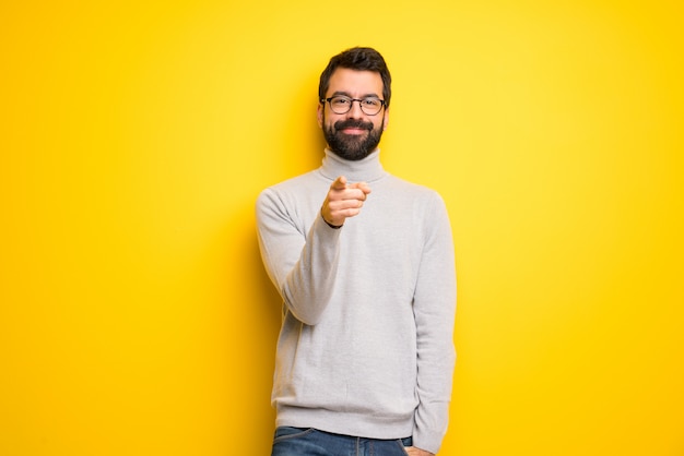 L'uomo con barba e collo alto punta il dito verso di te con un'espressione fiduciosa