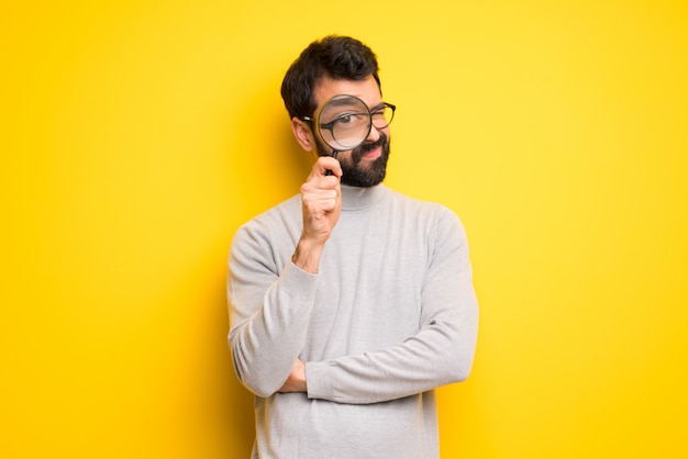 Man with beard and turtleneck taking a magnifying glass and looking through it