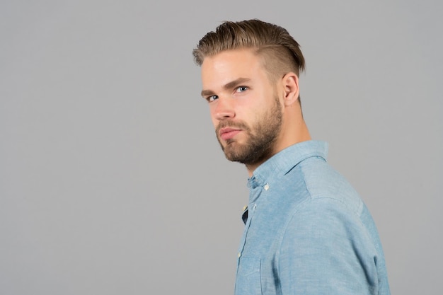 Man with beard on unshaven face skin. Bearded man in blue shirt. Fashion model with stylish hair grey background. Skincare and barber salon. Style or trend and hairstyle concept, copy space.