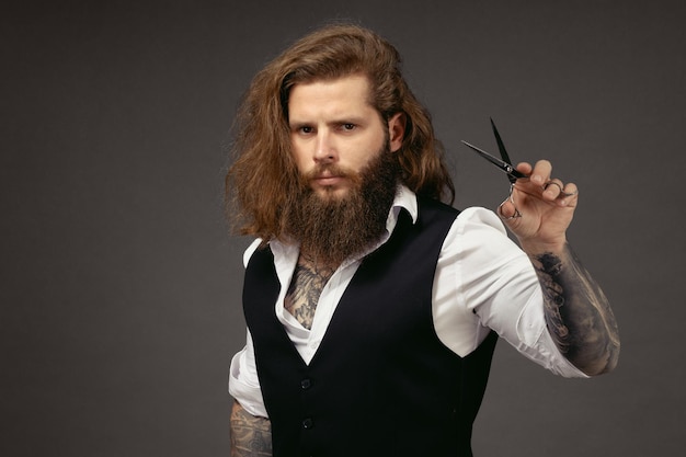 Man with a beard in a vest holds scissors in his hands