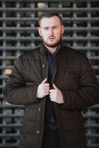 A man with a beard in a warm winter brown jacket poses for advertising of men's clothing in the winter. Advertising of men's clothing