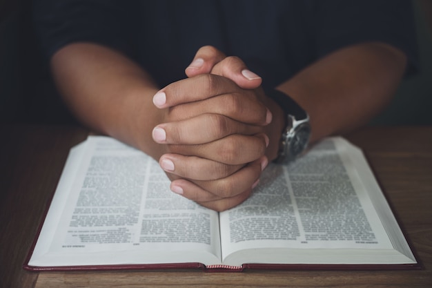 Photo man with bible praying, hands clasped together on her bible on wooden table.