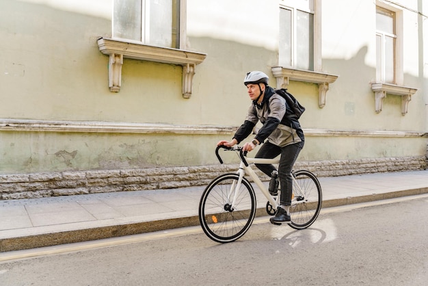 A man with a bicycle in a helmet delivering a backpack traveling in the city by mail takes