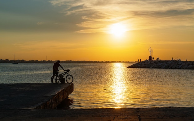 A man with a bicycle on the pier at sunset Rimini Italy