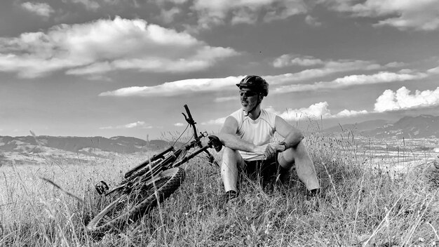 Foto uomo con una bicicletta seduto sulla terra contro il cielo