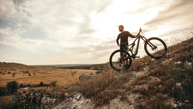 Man with bicycle standing on hill