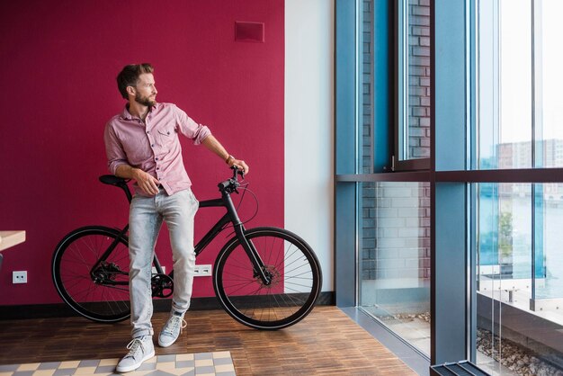 Man with bicycle standing in modern office looking out of window