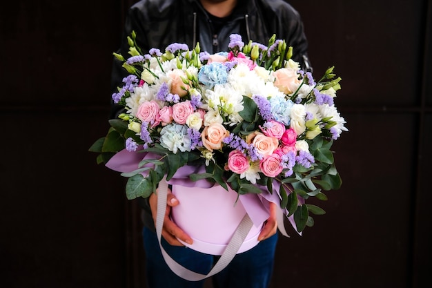 黒の背景に大きなカラフルな花束の花を持つ男