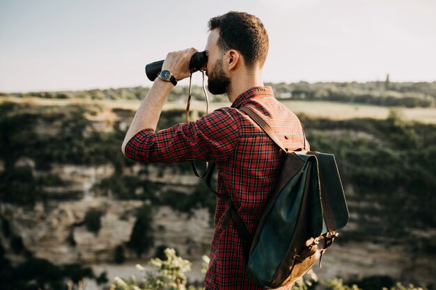 Man with binoculars standing on a cliff in mountains