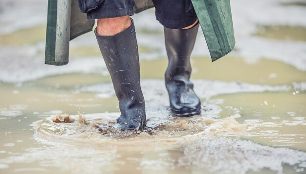 A man with black boots walks on a flooded road.