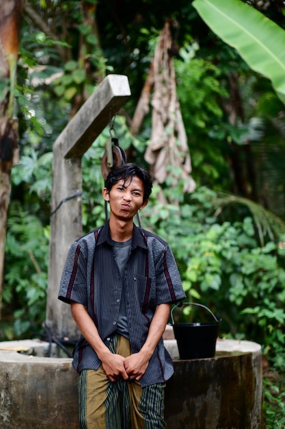 A man with a black ears sits on a wooden bench in a jungle.