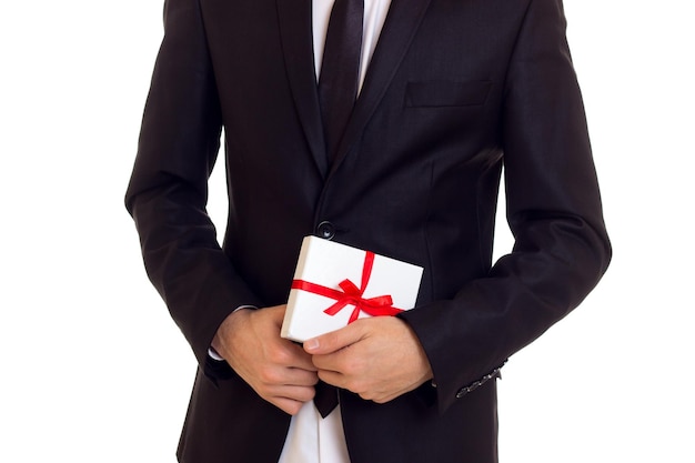 Man with black hair in white shirt and black tuxedo with tie holding a present on white background