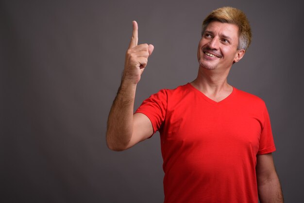 Uomo con capelli biondi che indossa la camicia rossa contro il muro grigio