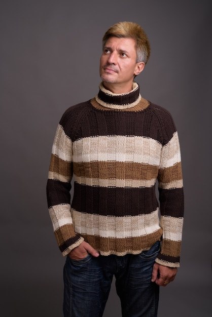 Man with blond hair wearing turtleneck sweater against gray wall