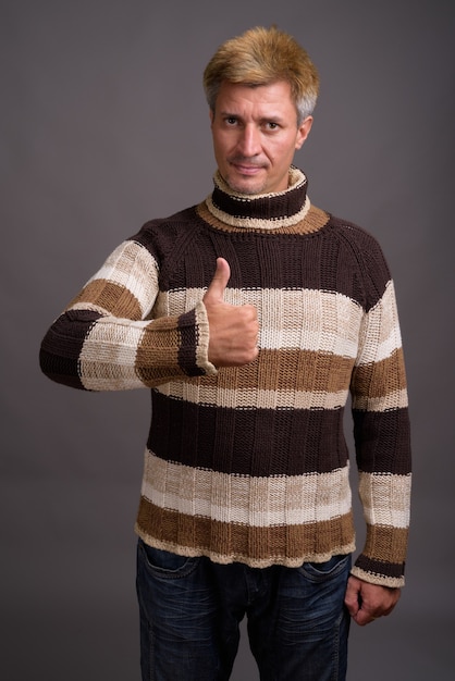 Man with blond hair wearing turtleneck sweater isolated against gray wall