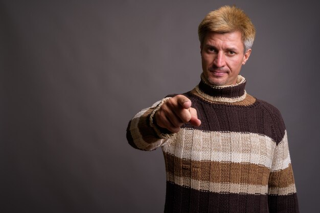 회색 벽에 고립 된 터틀넥 스웨터를 입고 금발 머리를 가진 남자