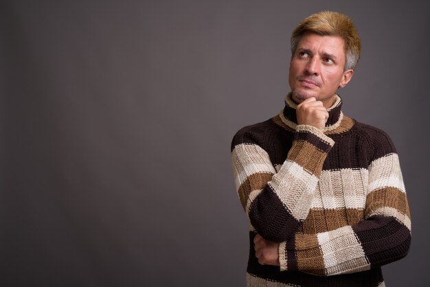 Man with blond hair wearing turtleneck sweater isolated against gray wall