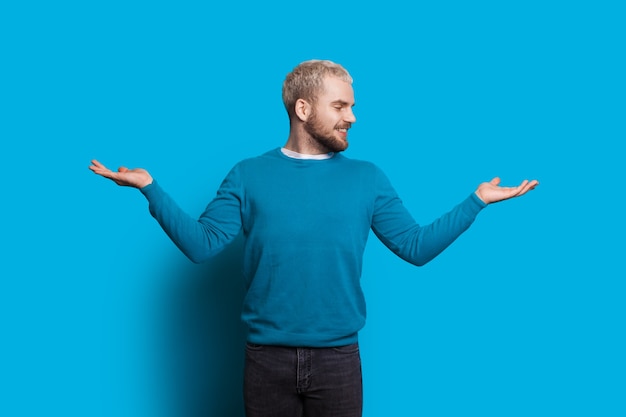  man with blonde hair and beard is gesturing a balance with his hands looking and smiling cheerfully on a blue wall