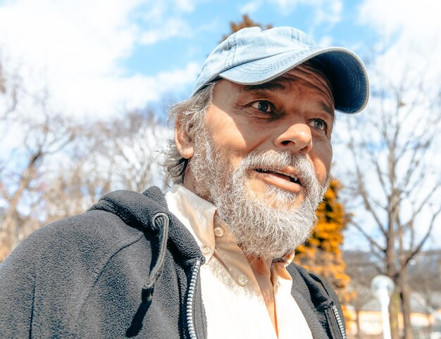 A man with a blue hat and a blue cap stands outside in the sunshine.