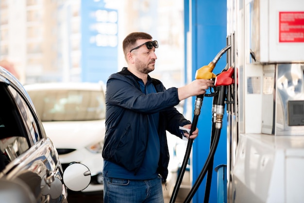 ガソリンスタンドで青いジャケットと濃いめがねをかけた男彼は車をいっぱいにするガソリンライフスタイル