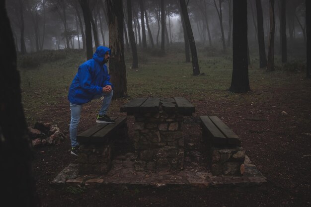 Man with blue raincoat walking through a foggy forest