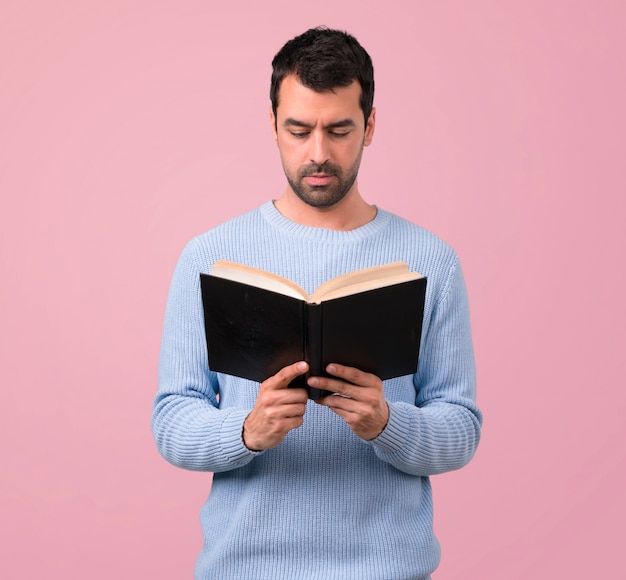 Man with blue sweater holding and reading a book 