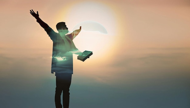 A man with a book in his hands is standing in front of a sunset.