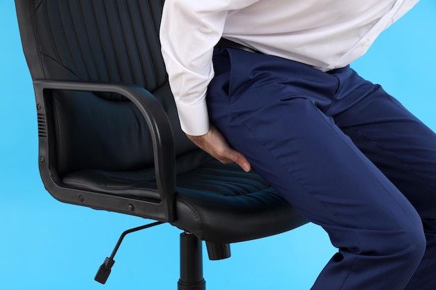 Man with bottom pain on blue background. Hemorrhoids concept