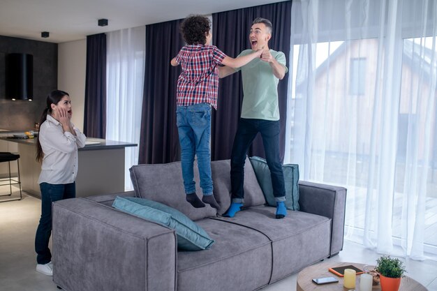 Man with boy jumping on couch and surprised woman