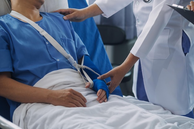 病院のベッドに横たわっているギプスで腕を骨折した男性緊急センターの治療は石膏であり、整形外科クリニックでのさらなる治療のためにスリングで吊るされています事故による怪我による患者の痛み
