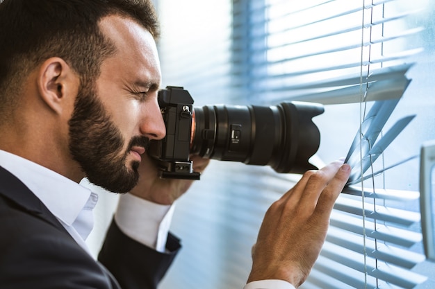 Foto l'uomo con una macchina fotografica che fotografa attraverso le persiane