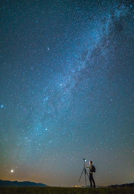 The man with a camera stand on the starry sky background. night time