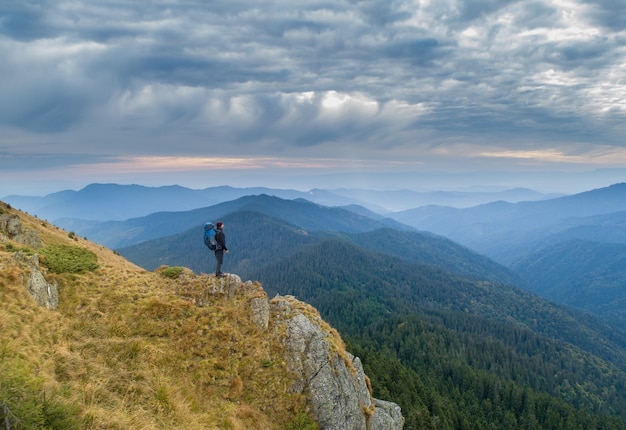 The man with a camping backpack standing on the rock