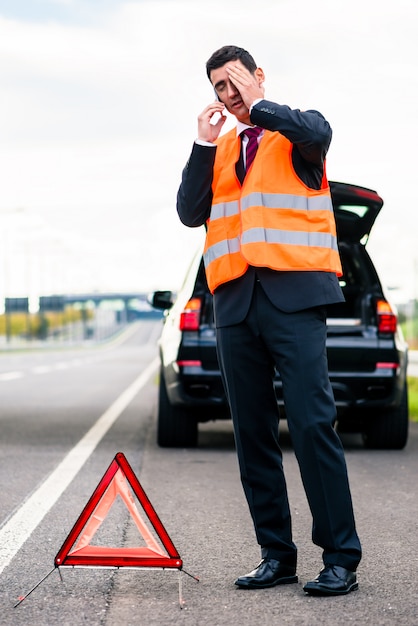 警告の三角形を建てる車の故障を持つ男