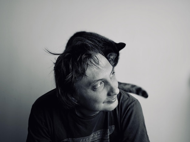 Foto uomo con il gatto sulla spalla contro il muro a casa