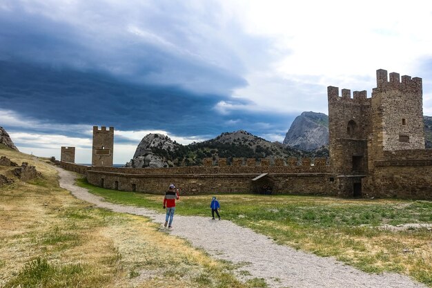 A man with a child against the background of an ancient Genoese fortress with a stormy sky Sudak