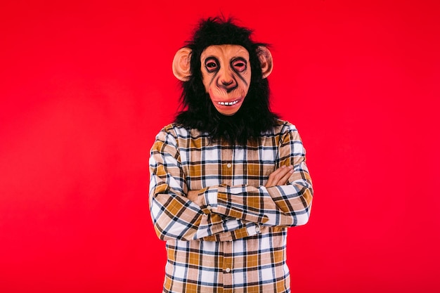 Foto uomo con maschera scimmia scimpanzé e camicia a quadri con braccia incrociate su sfondo rosso