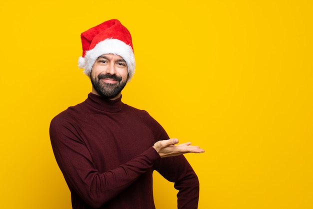 に向かって笑顔を見ながらアイデアを提示する分離の黄色の背景の上のクリスマス帽子の男